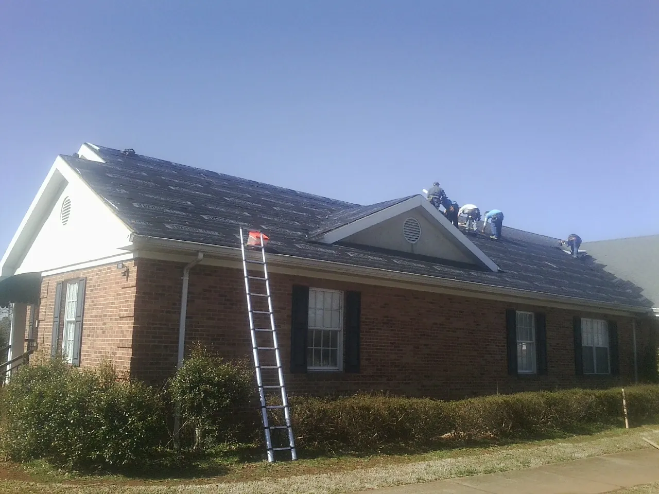 Crew tearing shingles off a brick ranch roof with a ladder set — Emergency Roof Repair work by our crew in Bandon