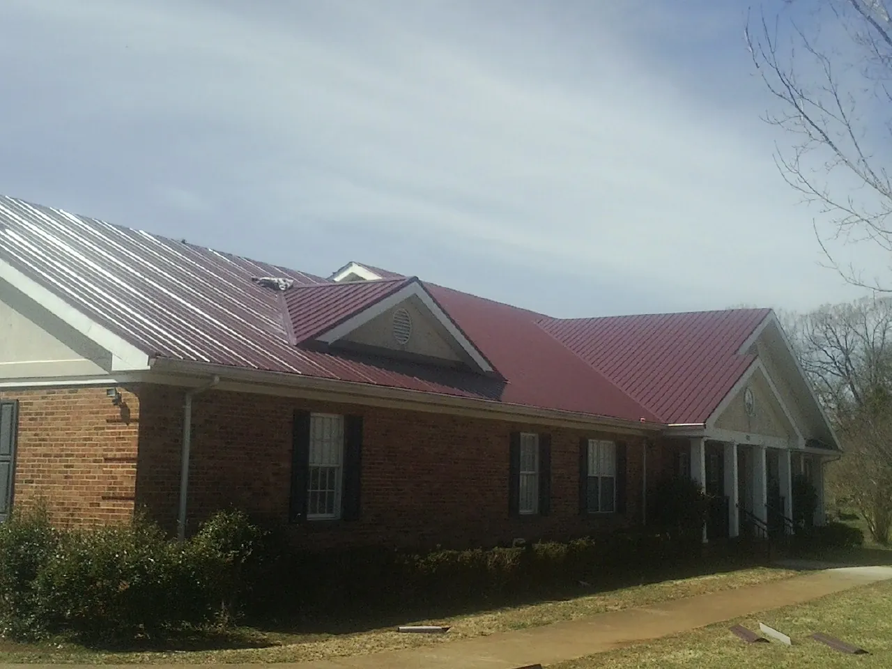 Red metal roof with gabled entries on a long brick building, from a Hail Damage Roof Repair job in Bandon