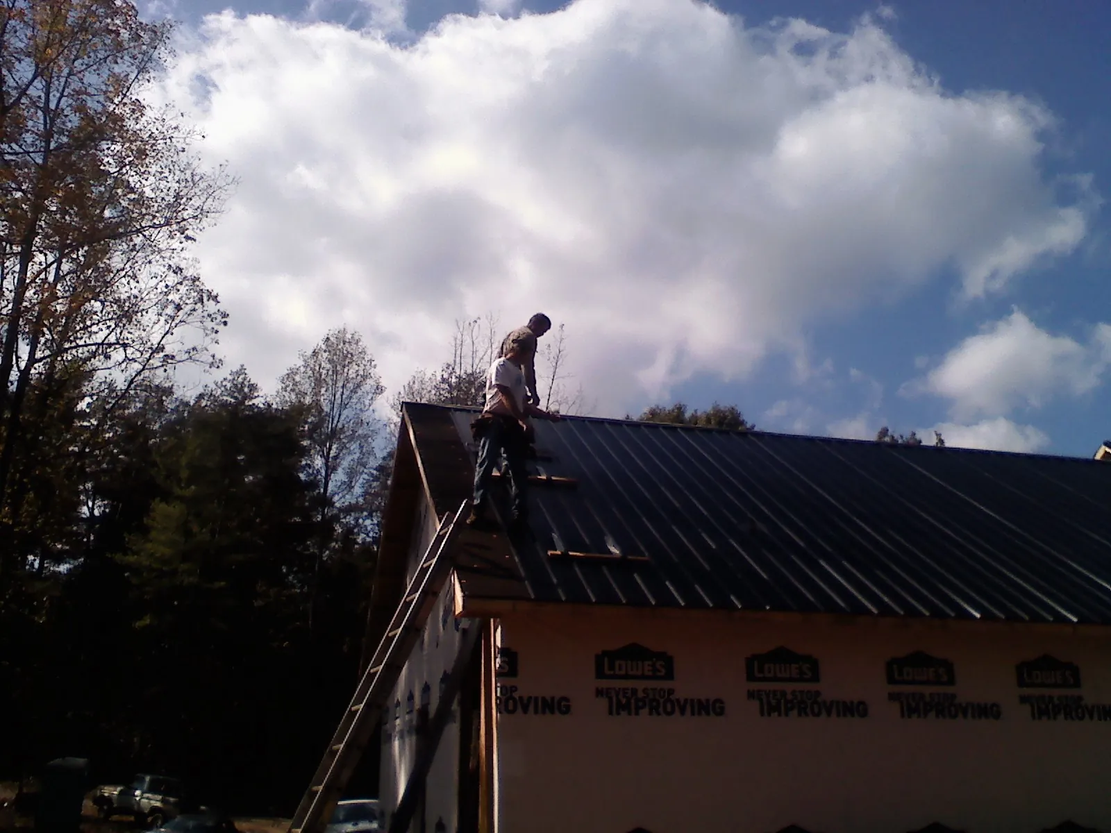 Roofer fastening dark metal panels high against a cloudy sky, from a Roof Inspection job in Bandon