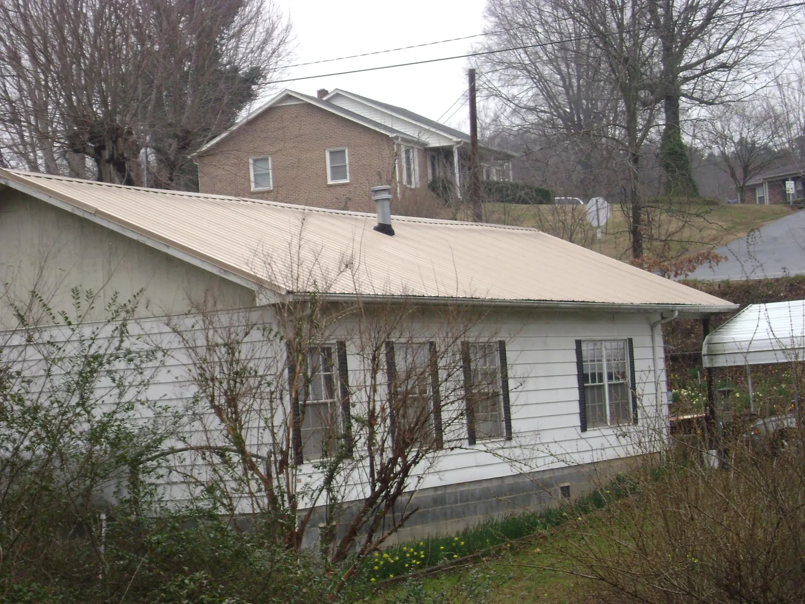 Tan metal roof on a white sided house set into a hillside — Commercial Roofing by Roofing Brothers in Bandon